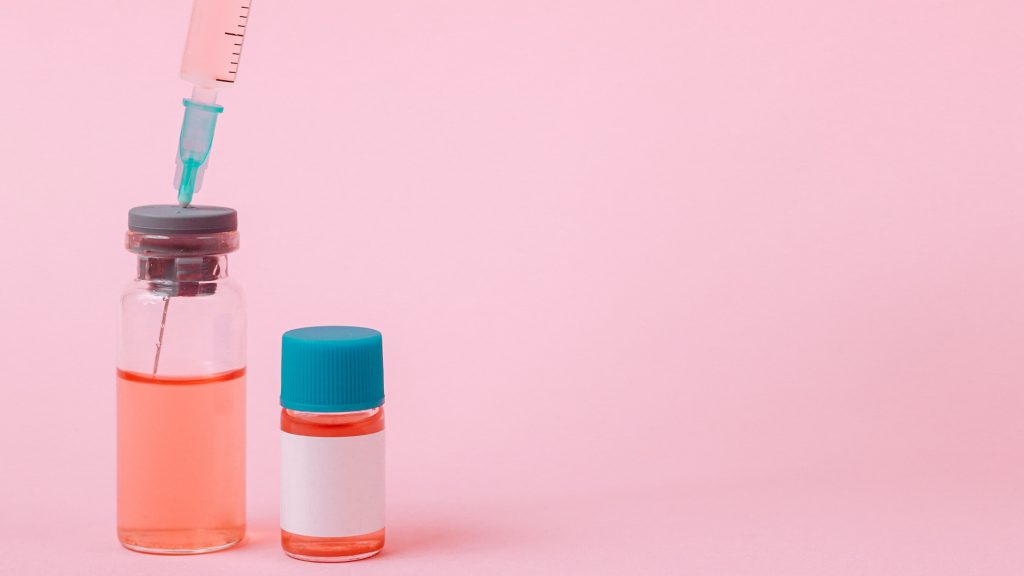Pink background with syringe collecting fluid from test container vaccine image