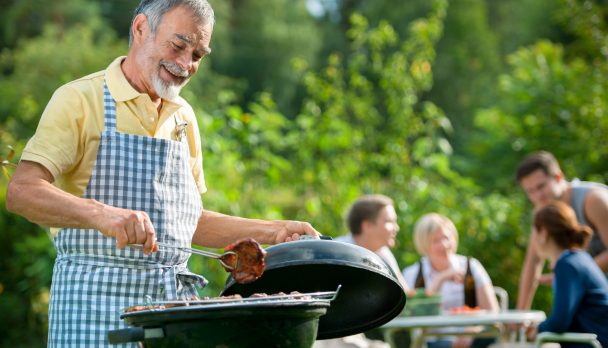 Older man barbecuing outside with family in background